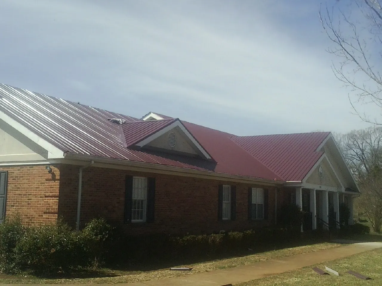 Red metal roof with gabled entries on a long brick building, from a Hail Damage Roof Repair job in Verona
