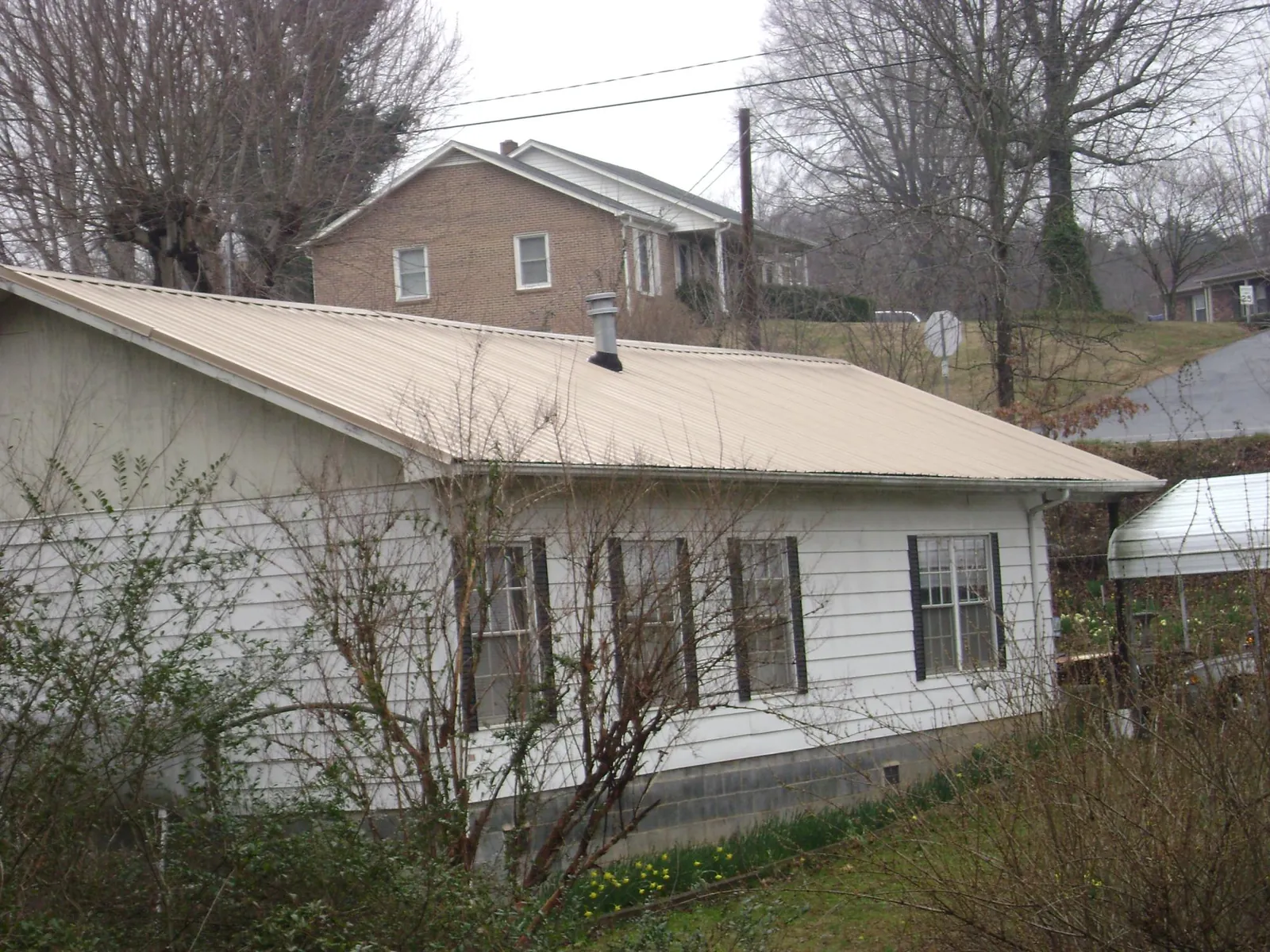Tan metal roof on a white sided house set into a hillside — Commercial Roofing by Roofing Brothers in Verona